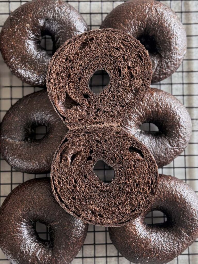 Brown pumpernickel bagels 6 on a cooling rack with one bagel cut in half