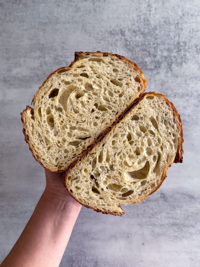 Hand holding sourdough loaf cut open in half showing open crumb